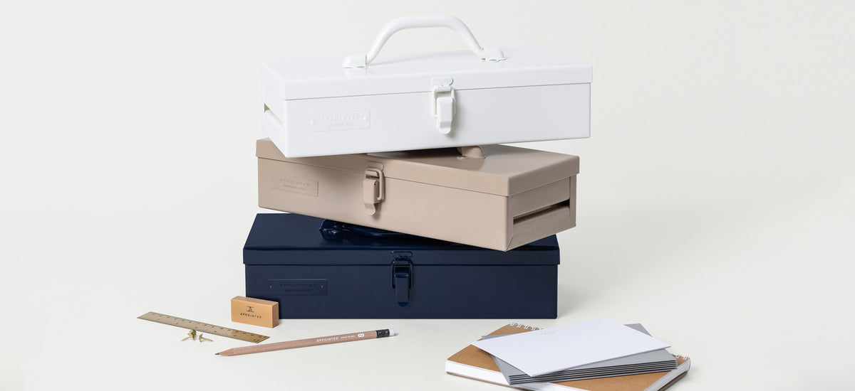 Three American-made toolkits are stacked on top of eachother with desk accessories on a cream-colored background